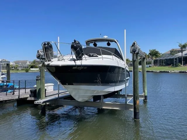 2019 Monterey 295 boat on lift, docked by waterfront homes under clear blue sky.