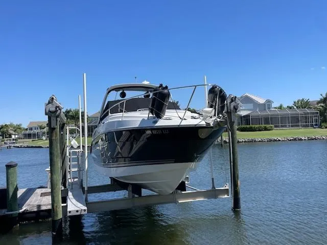 2019 Monterey 295 boat on lift, docked by waterfront homes under clear blue sky.