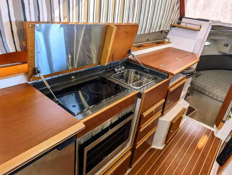 2022 Cutwater C-32 Coupe LE galley with stove, sink, and wooden cabinetry.